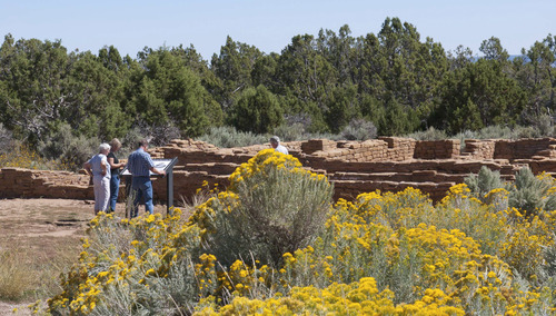 Three people reading interpretive sign in from of a low, ancient, stone-masonry room walls.