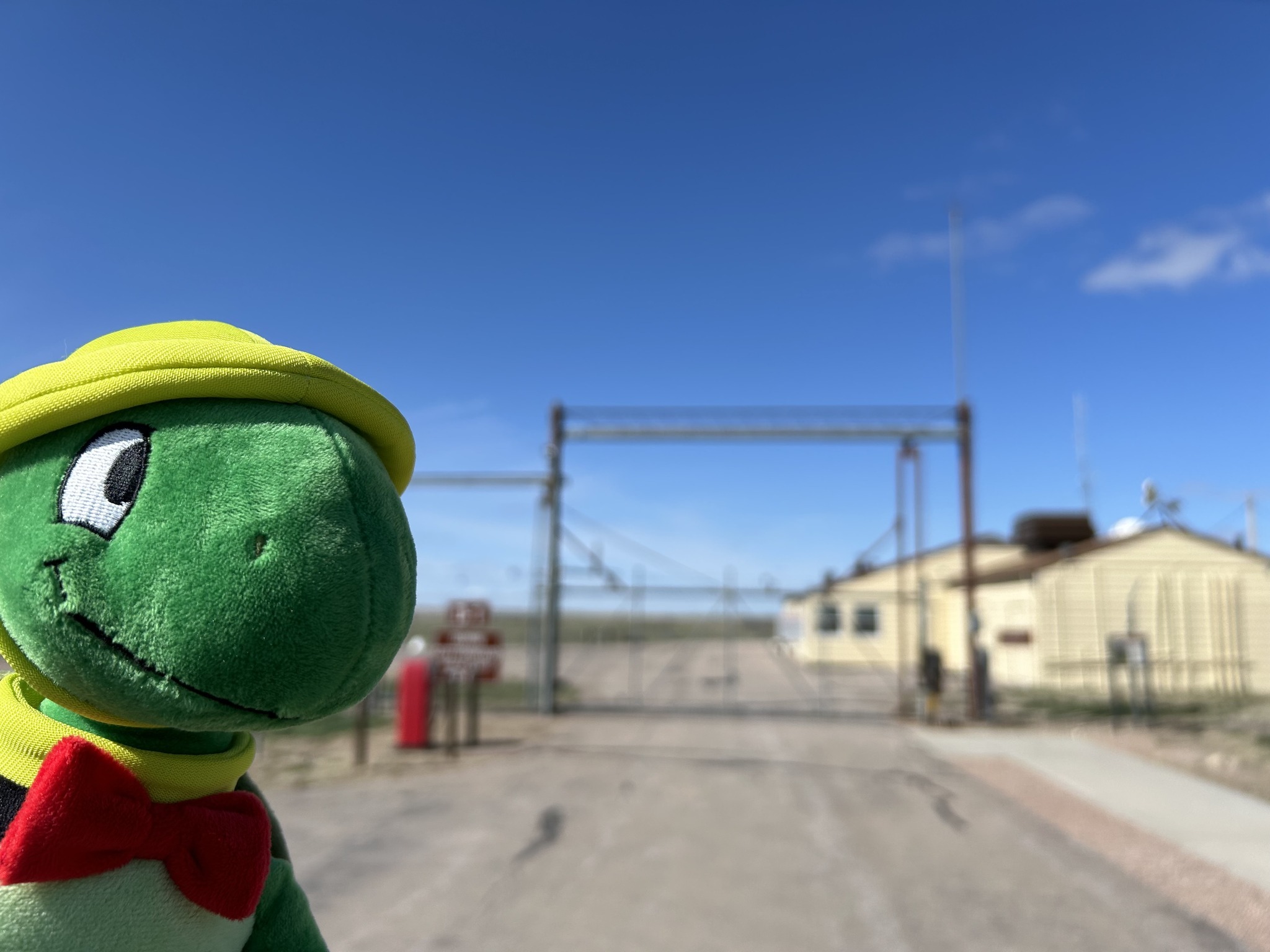 a beige farmhouse on the prairie surrounded by a large fence with a red gas pump outside. 