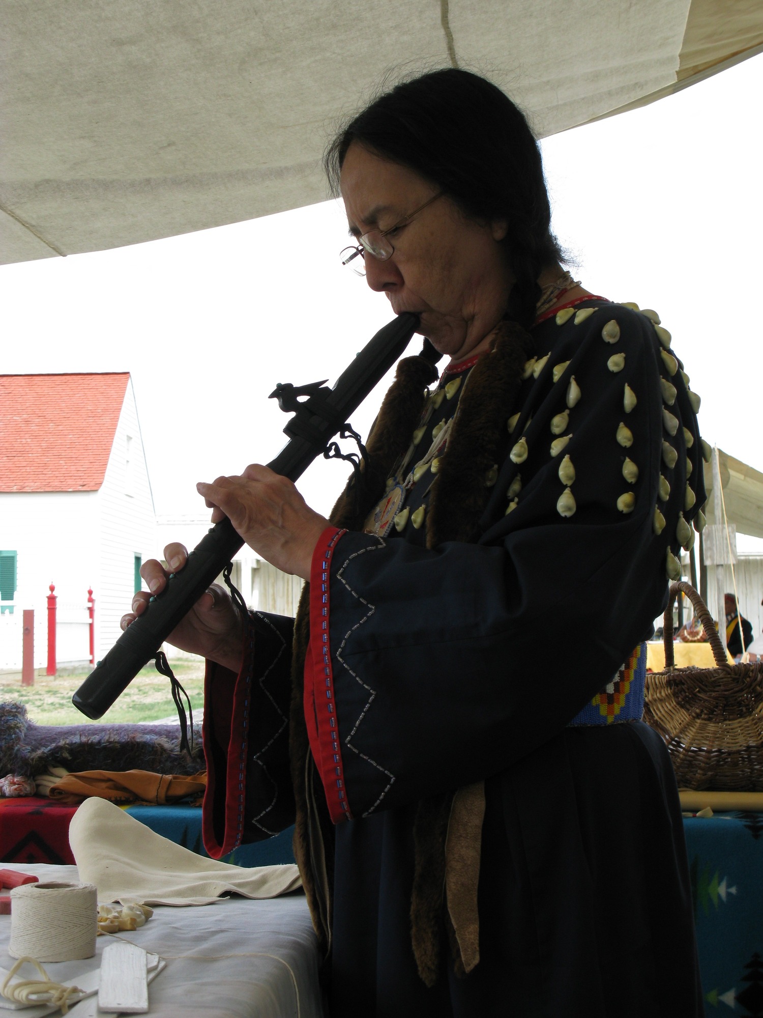 A woman in traditional American Indian dress plays a flute