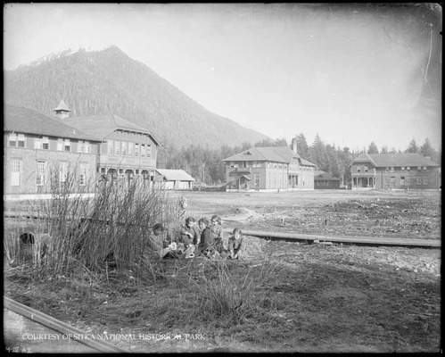 Five female students sitting in the foreground on the lawn of the Sheldon Jackson School Campus.
