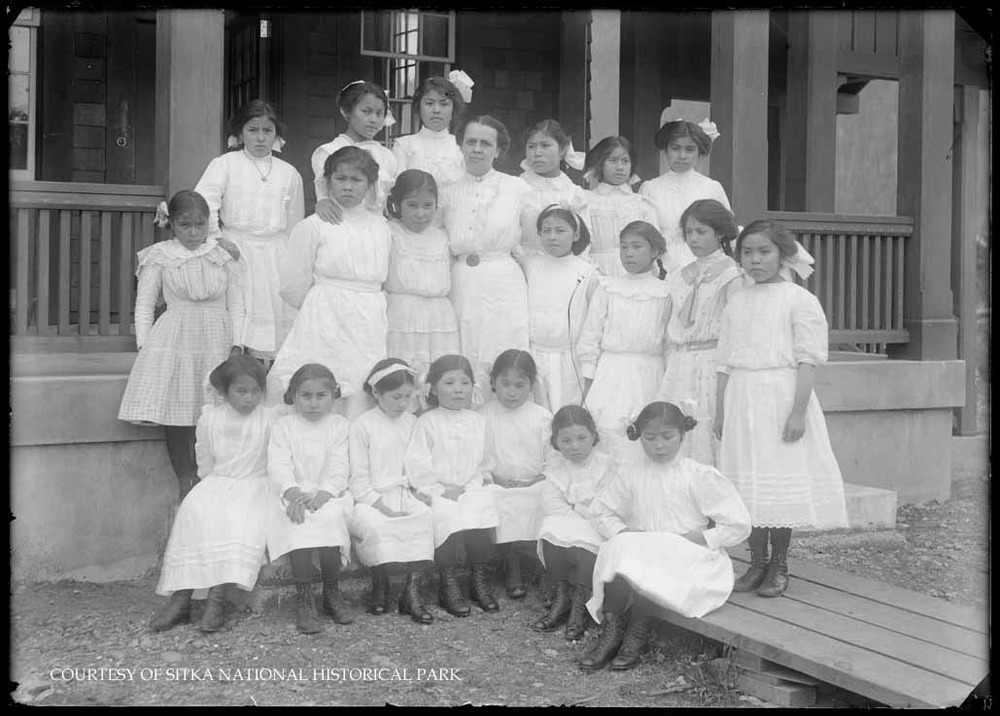 Two images of a group of 62 Native school children with 1 white female teacher posed for a class picture.