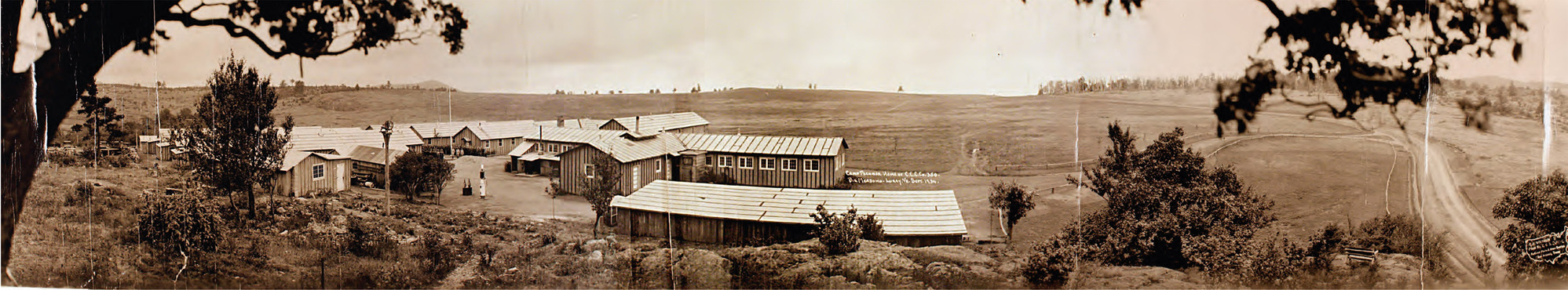 CCC Camp No. 2 is a cluster of buildings to the left of a road. A rolling meadow extends into the distance. 