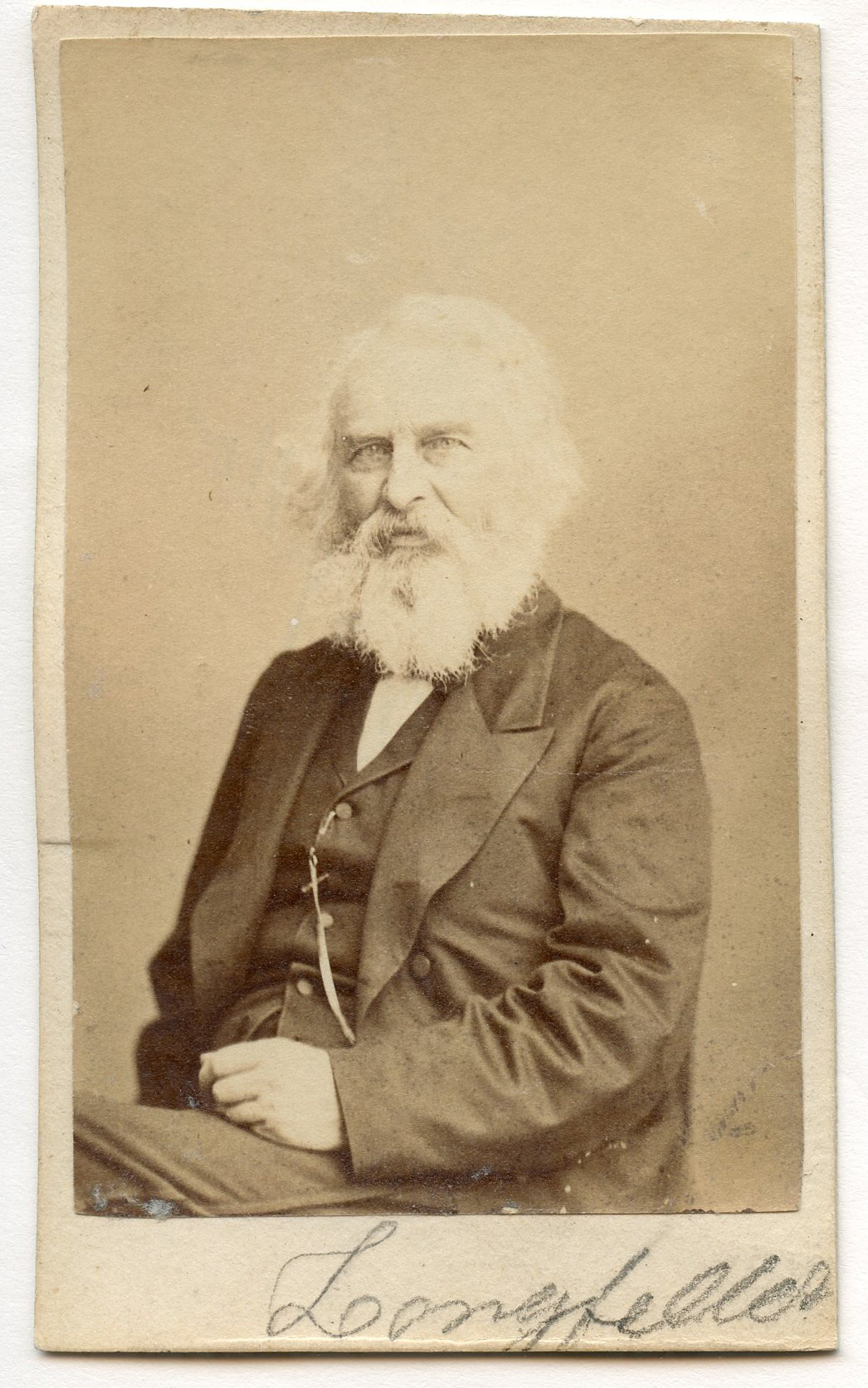 Henry Wadsworth Longfellow sitting with his body angled to his right and his face looking towards the viewer. He wears formal attire and has white chin-length hair and a full white beard.