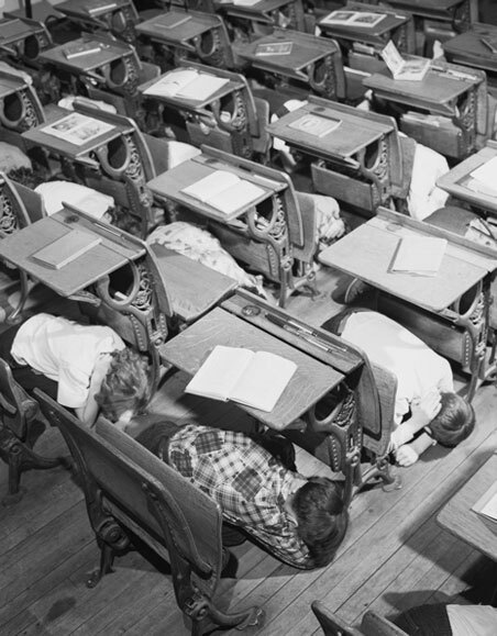 Black and white photo of students crouching under their wooden desks