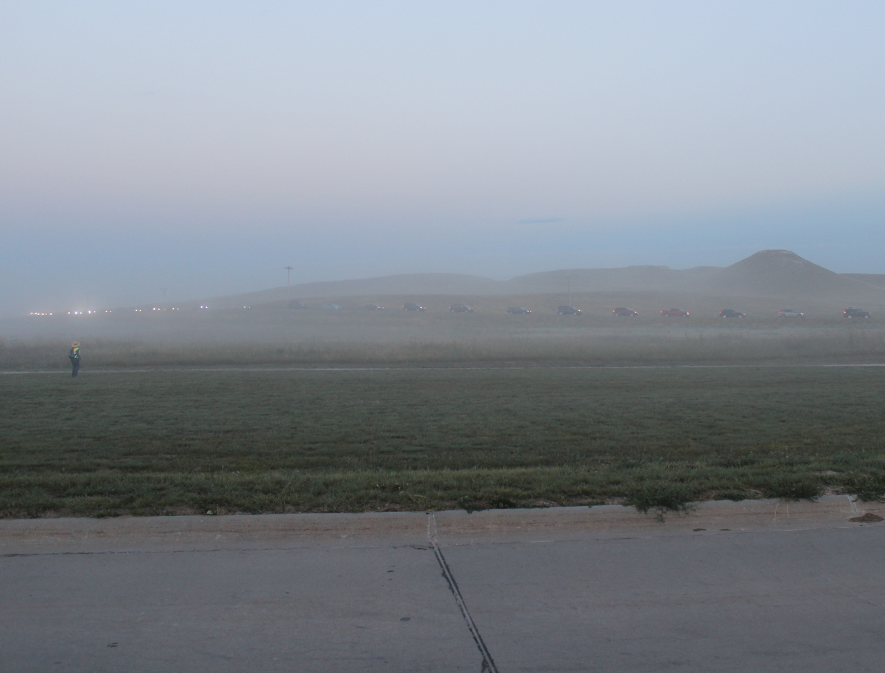 Long line of cars in distant fog past a grassy area