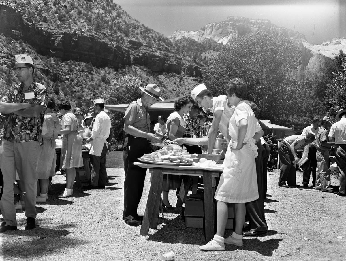 Superintendent Frank R. Oberhansley being served at barbecue following the dedication program at the Mission 66 Visitor Center and Museum. Utah Parks Company (Union Pacific Railroad) staff serving park employees and visitors near Oak Creek residential area. Over 600 people attended ceremony.