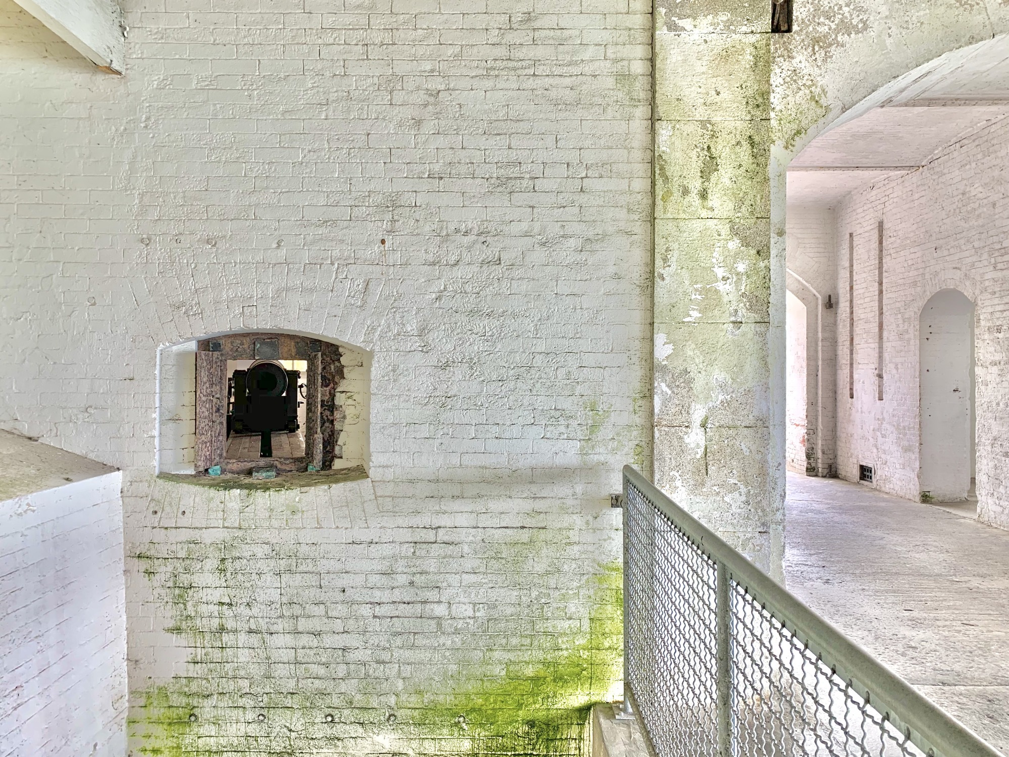 A small arched opening reveals a black cannon sticking out of a white brick wall.