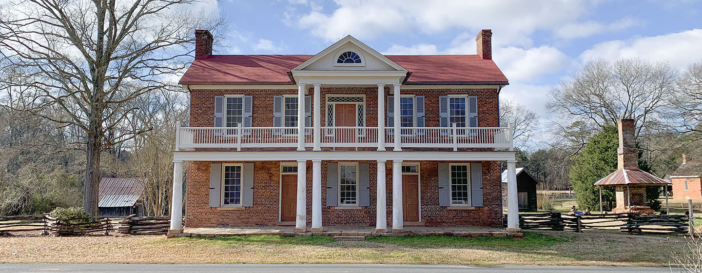 A large two-story brick house with two-story porch and light blue shutters.