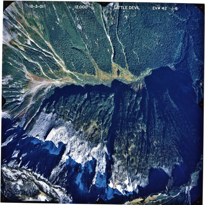 Color aerial photograph of glaciated mountain peak with forested valleys below.