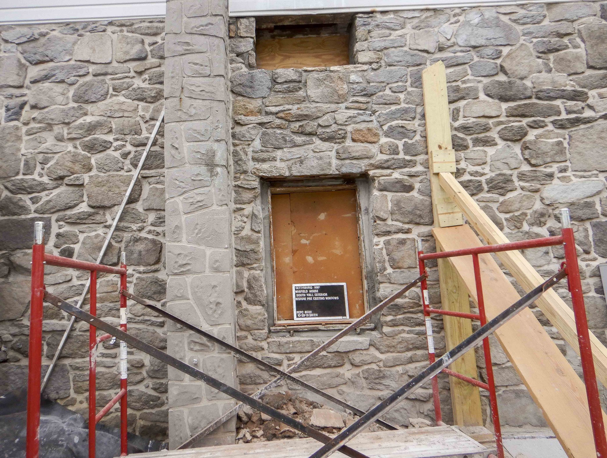 The windows on the south wall exterior after the restoration process had been finished. There is a small window at the top of the house and a normal sized window a couple feet below. Both have plywood placed behind them. 
