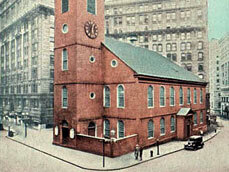 Colorized archival image of a brick church with a tall steeple forming the narthex entrance. Steeple tower has a clock. Nave is a two story brick structure with a pitched roof. Windows are arched.