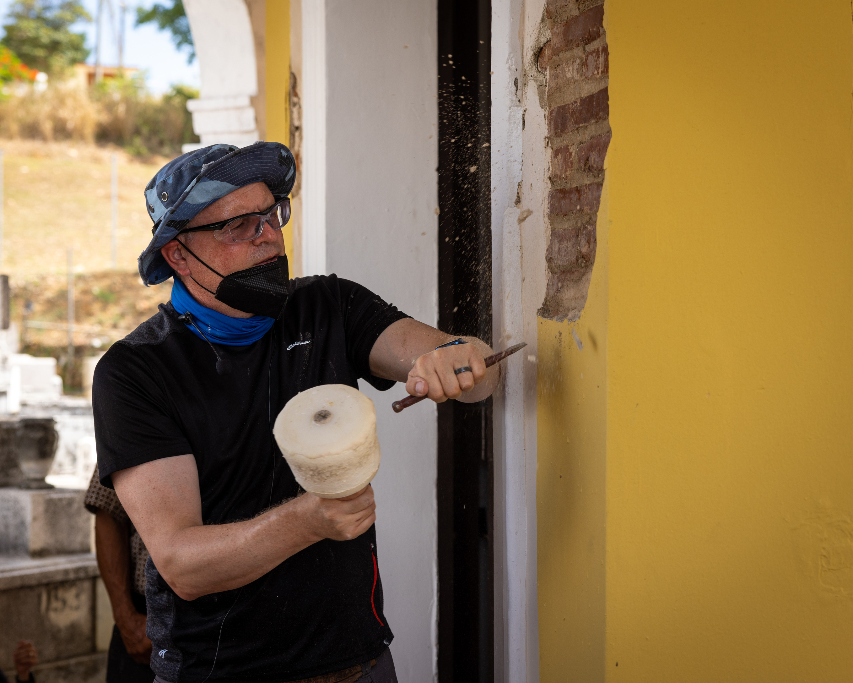 Simeon Warren removing loose plaster from from exterior or cemetery chapel using a mallet and chisel
