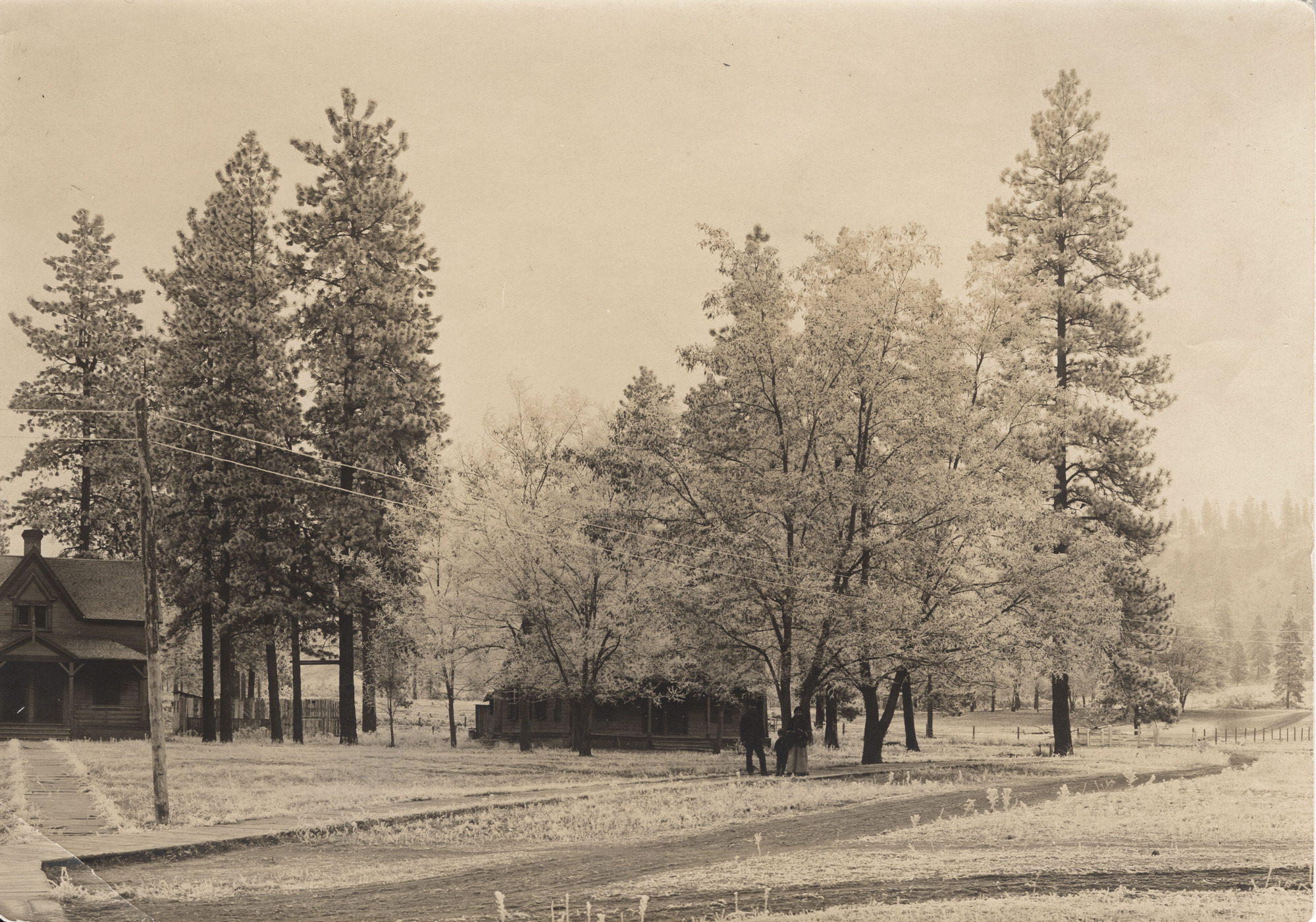Sepia toned photograph of a family among trees and buildings next to a road