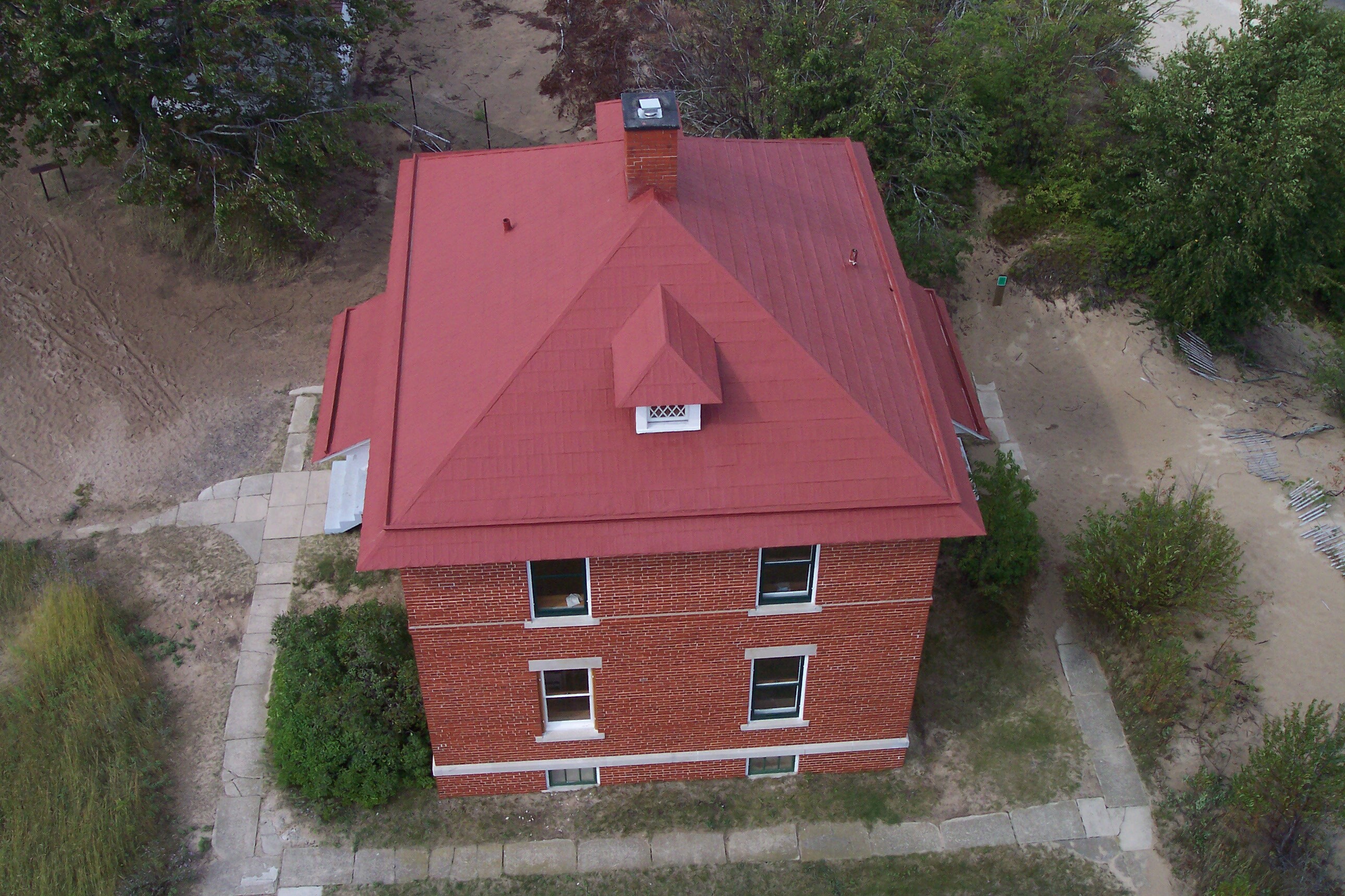 Looking down from the top of the lighthouse to the red roof of the square two story brick building