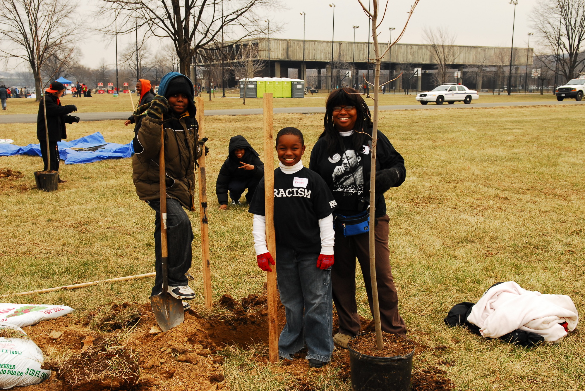 Four children smile for the camera as they stand next to a tree they just planted.