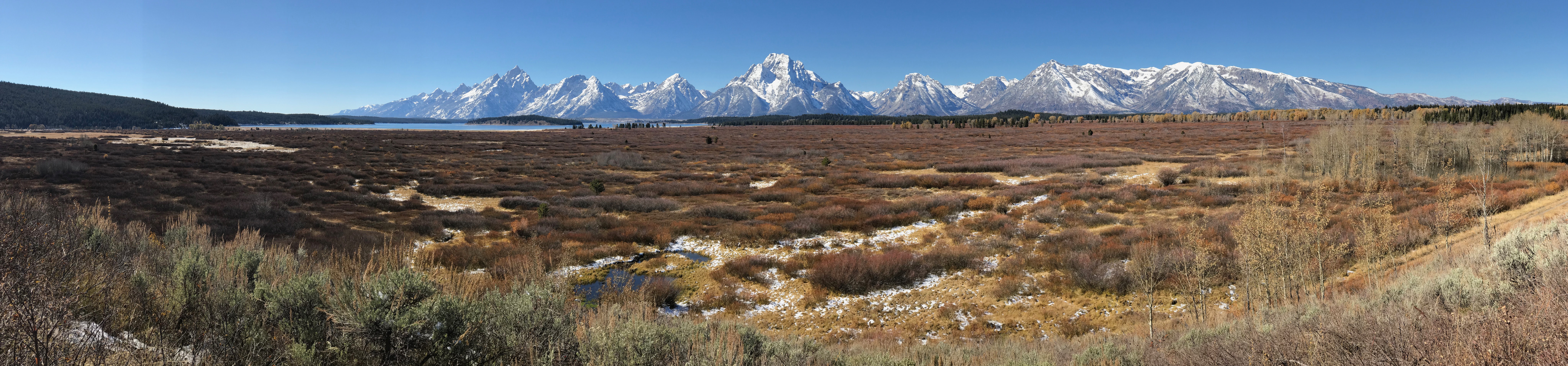 Brownish-orange wetlands and water cover a sweeping landscape, with a bit of Jackson Lake visible at base of the snow-covered peaks of the Teton Range