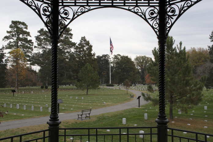 Two wrought iron columns frame a view of thousands of headstones and grave markers along with a handful of trees on an overcast morning. 