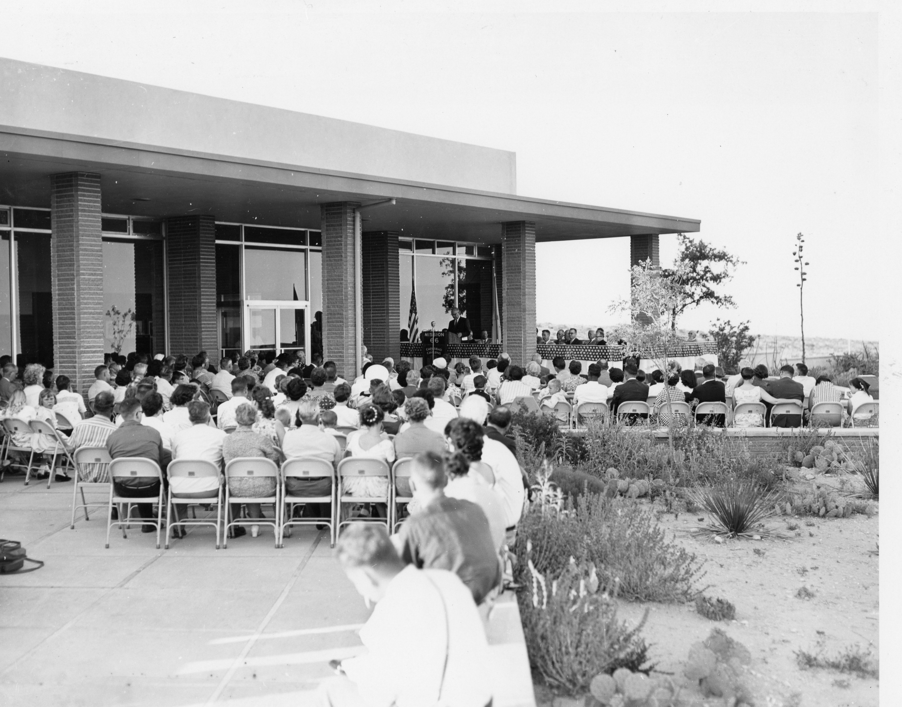 A black and white photograph of many people sitting at a dedication ceremony for the new visitor center.