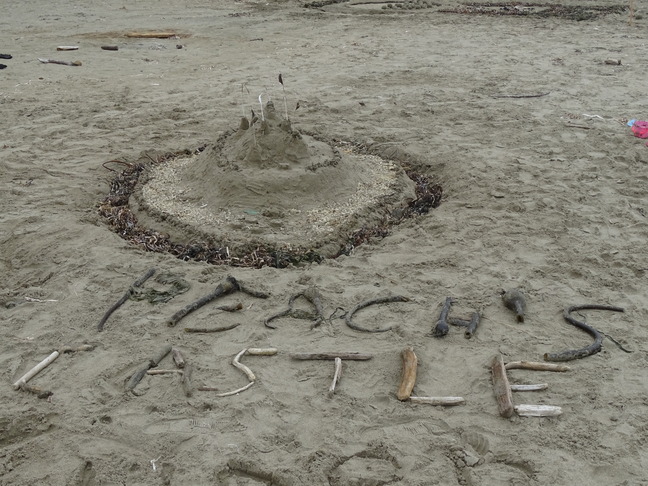 A sand sculpture of a small circular castle with seaweed and sticks in the foreground spelling out "Peach's Castle."