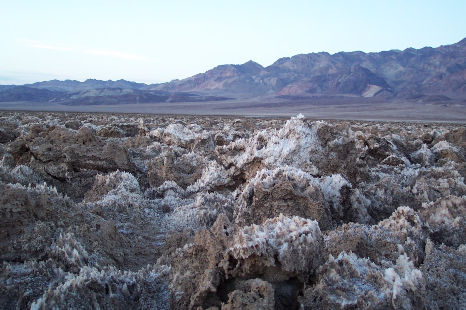 A crust of hard salt and mud forming spires and ridges at ground level, with mountains in the distance.