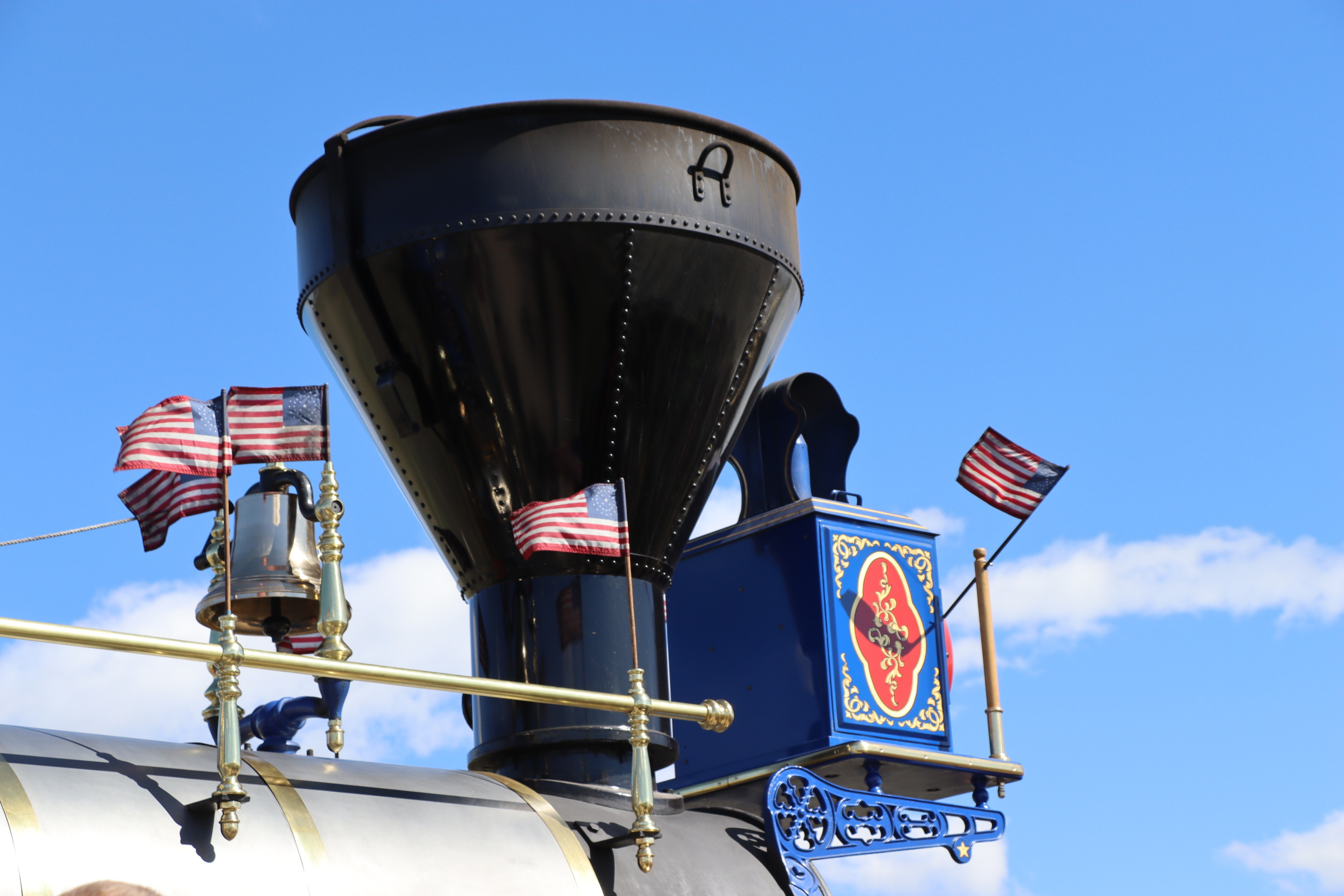 Bell, smokestack, and 37-star American flags against the blue sky.
