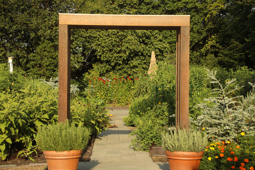 The entry way into a large garden with various plants, flowers, and vegetables. 