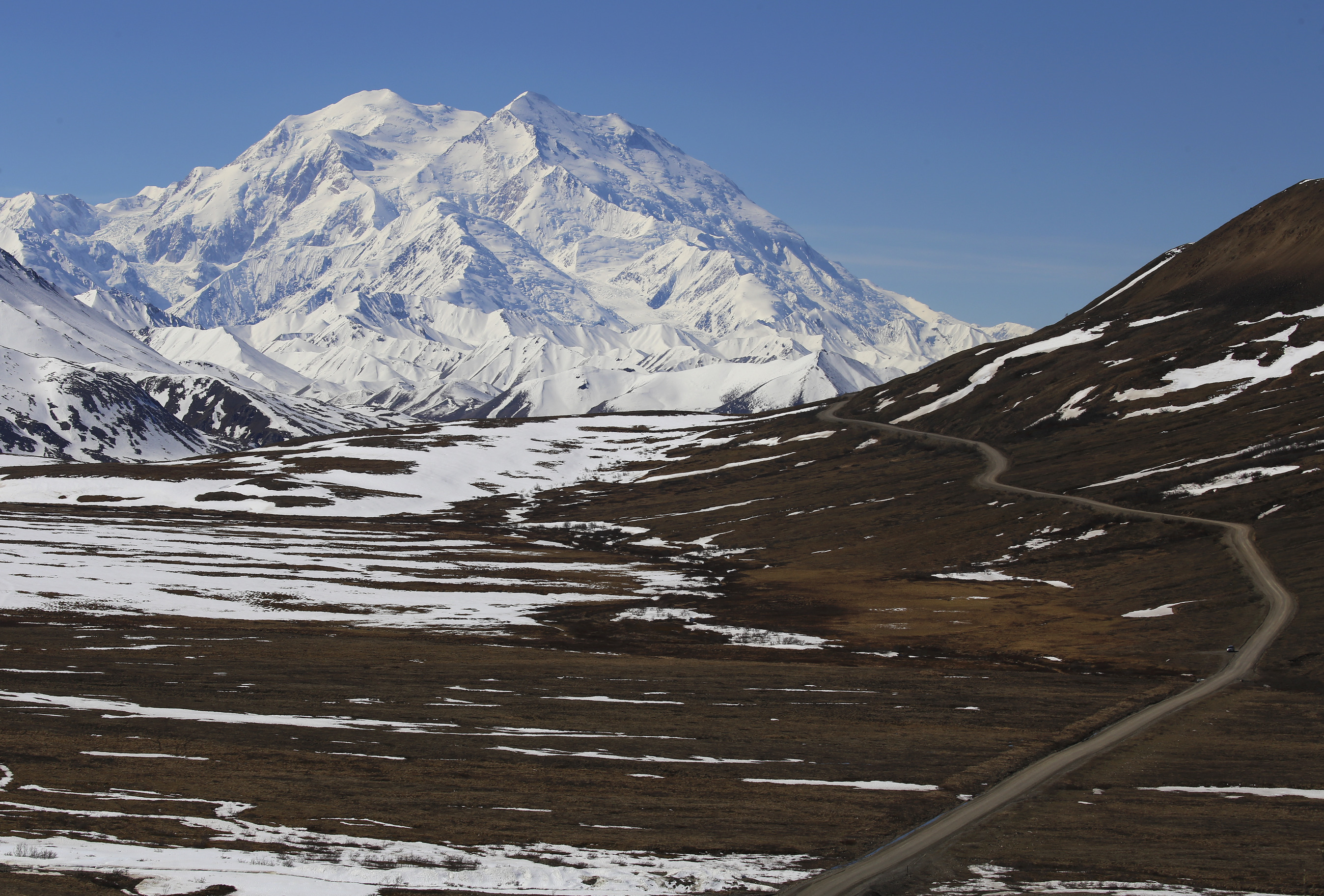 brown landscape with a dirt road traveling through it toward a distant, snowy mountain