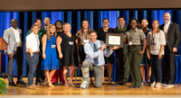 A group of fifteen smiling park rangers and staff accepts an award on a stage with the Director of the Park Service. 