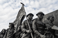 A bronze statue of a multiple people in world war I. One of the men holds a large American flag. 