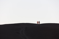 a family appearing very small as they hike down a bare, black cinder cone