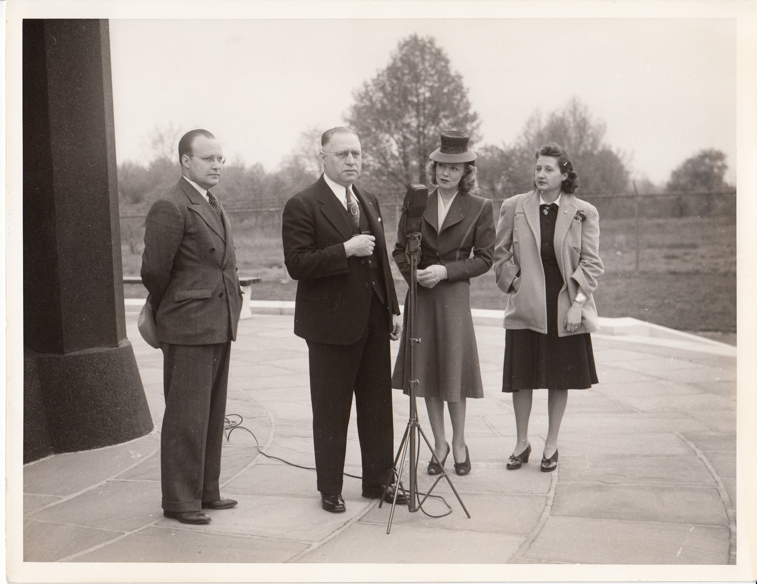 Unidentified man at microphone at Menlo Park tower, Rita Johnson and others looking on.