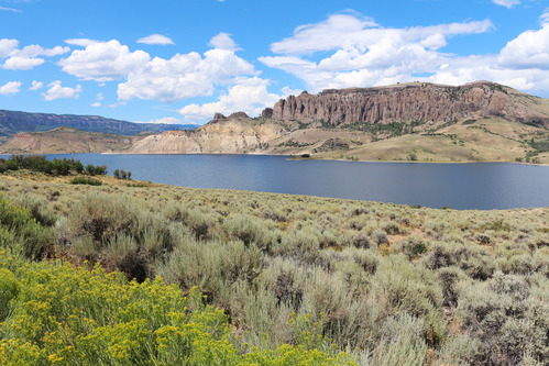 A large body of water with vegetation in the foreground. Large pinnacle spires are in the background across the water