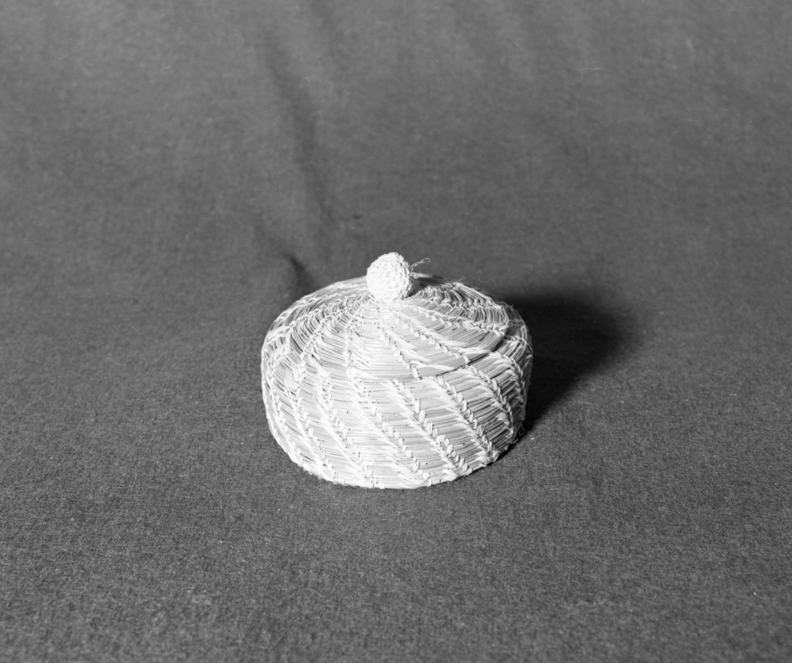 Marie Rozier Collection, Catalog No. 234. Object: Pine needle basket. Dimensions: 5 1/2" diameter. Materials: pine needles, raffia, felt. Collection History: Bought at Wilder's Stationery in Sonora in 1973. Made by Thyllie Wolf, who was born in 1891. Photographed by Michael Dixon, December 1982. Catalogued by Craig Bates and Barbara Beroza. Yosemite Collections, National Park Service.