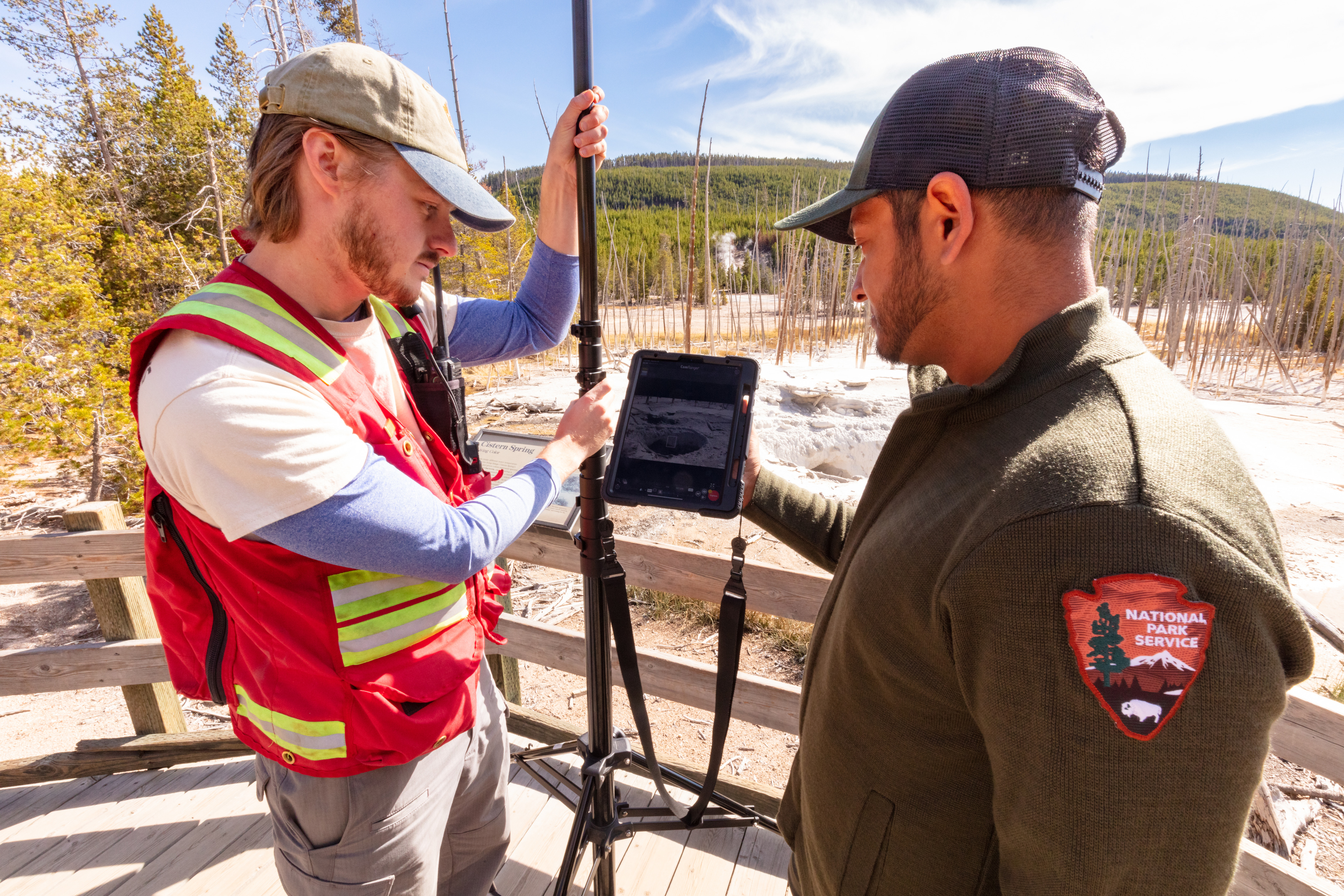 A uniformed man and another man talk next to a flat screen in the geyser basin