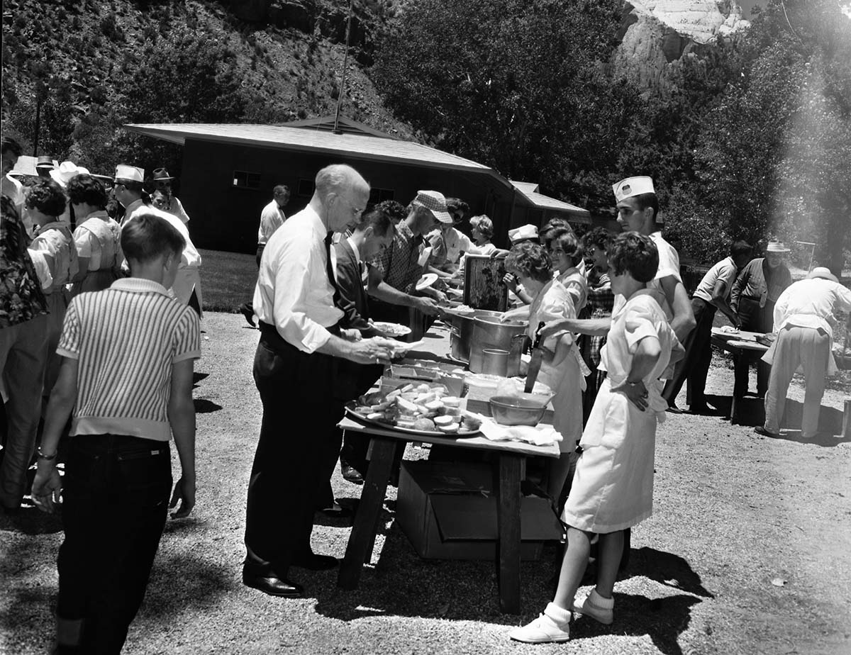 Superintendent Frank R. Oberhansley being served at barbecue following the dedication program at the Mission 66 Visitor Center and Museum. Utah Parks Company (Union Pacific Railroad) staff serving park employees and visitors near Oak Creek residential area. Over 600 people attended ceremony.