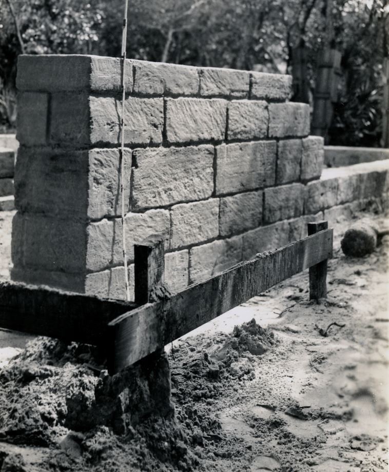Black and White photo. a portion of the stone wall.  Measuring stick, wood supports