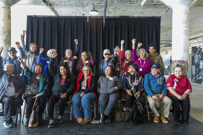A group of 18 people sitting and standing, many with one fist held high