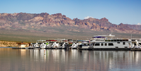 row of houseboats reflected in water with mountains in distance