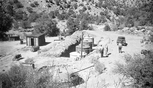 Men standing next to open trench with four underground storage tanks set in place in the Oak Creek Maintenance Area. Tanks were obtained from war surplus, used for storage of road oil. Installation is faulty in that the tanks were set too low for loading. Tanks will have to be raised about three feet to facilitate loading out. Machinery and structures in background.