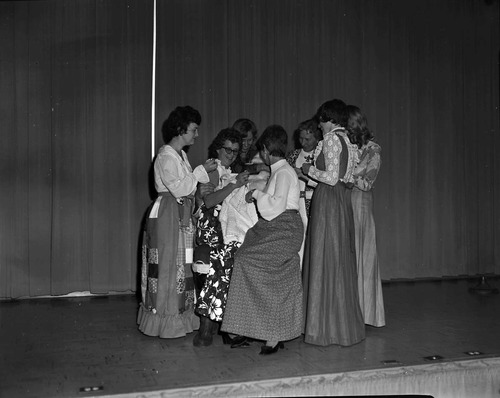 Christmas holiday party, 1976. Group of women sit on Santa's lap on stage in the Visitor Center auditorium.