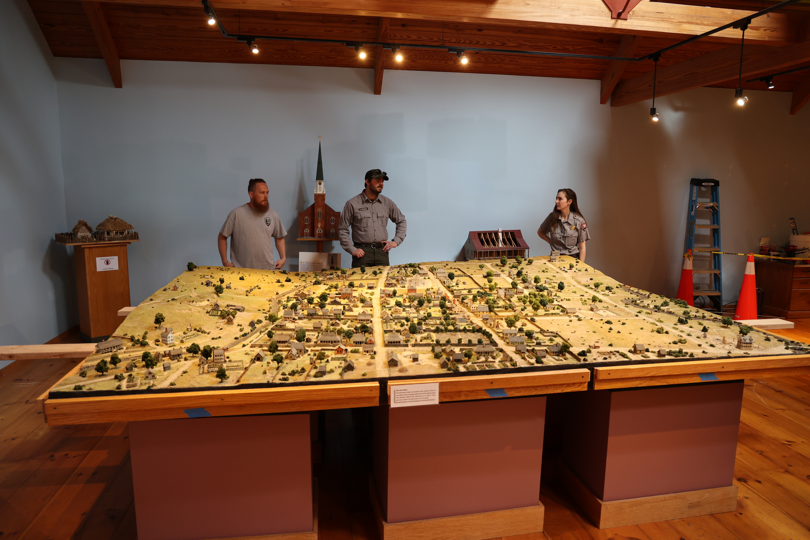 Three members of the park staff gather around a large diorama planning how best to move it, within a bluish grey room.