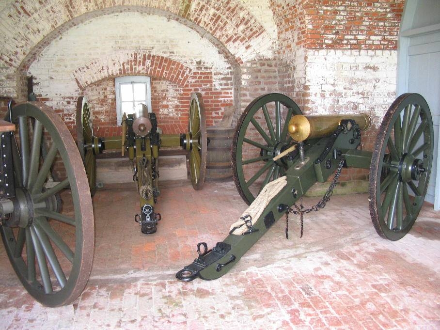 Three large cannons in a brick room. 