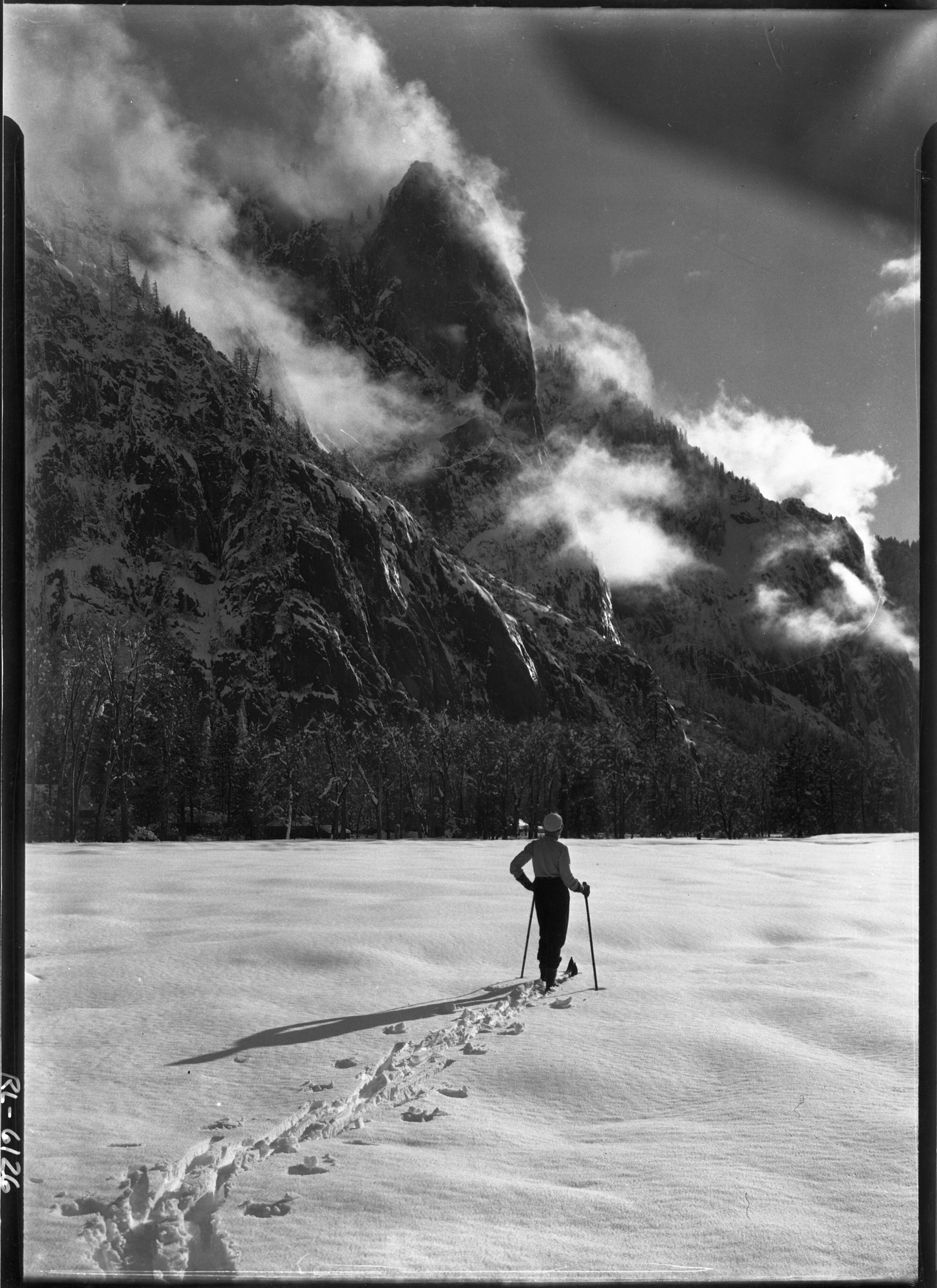 Miss Emely Hoag and Sentinel Rock. Also on the original envelope was a statement possibly for public information: Winter visitors find a different Yosemite with broad meadows covered with snow and tufts of clouds floating around the familiar landmarks after snowstorms. Also note cloud in upper right corner was produced by holding cotton over corner during exposure. The negative will not have clouds in the upper right hand corner.