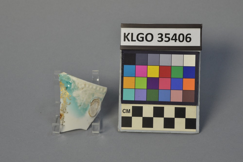 color photo of small white ceramic fragment with blue  and gold painted detailing