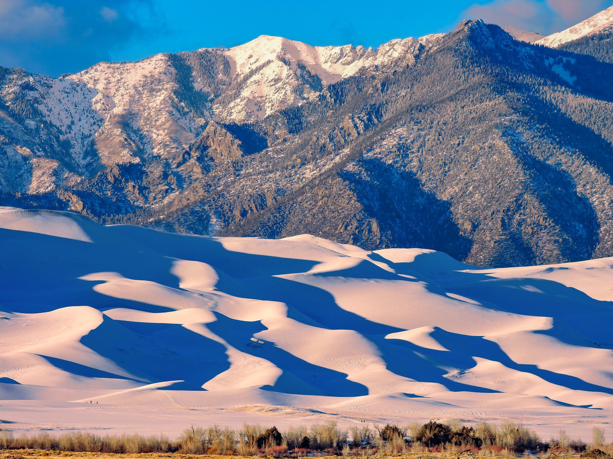 Snowy dunes are lit up by late afternoon sun below a mountain ridge.
