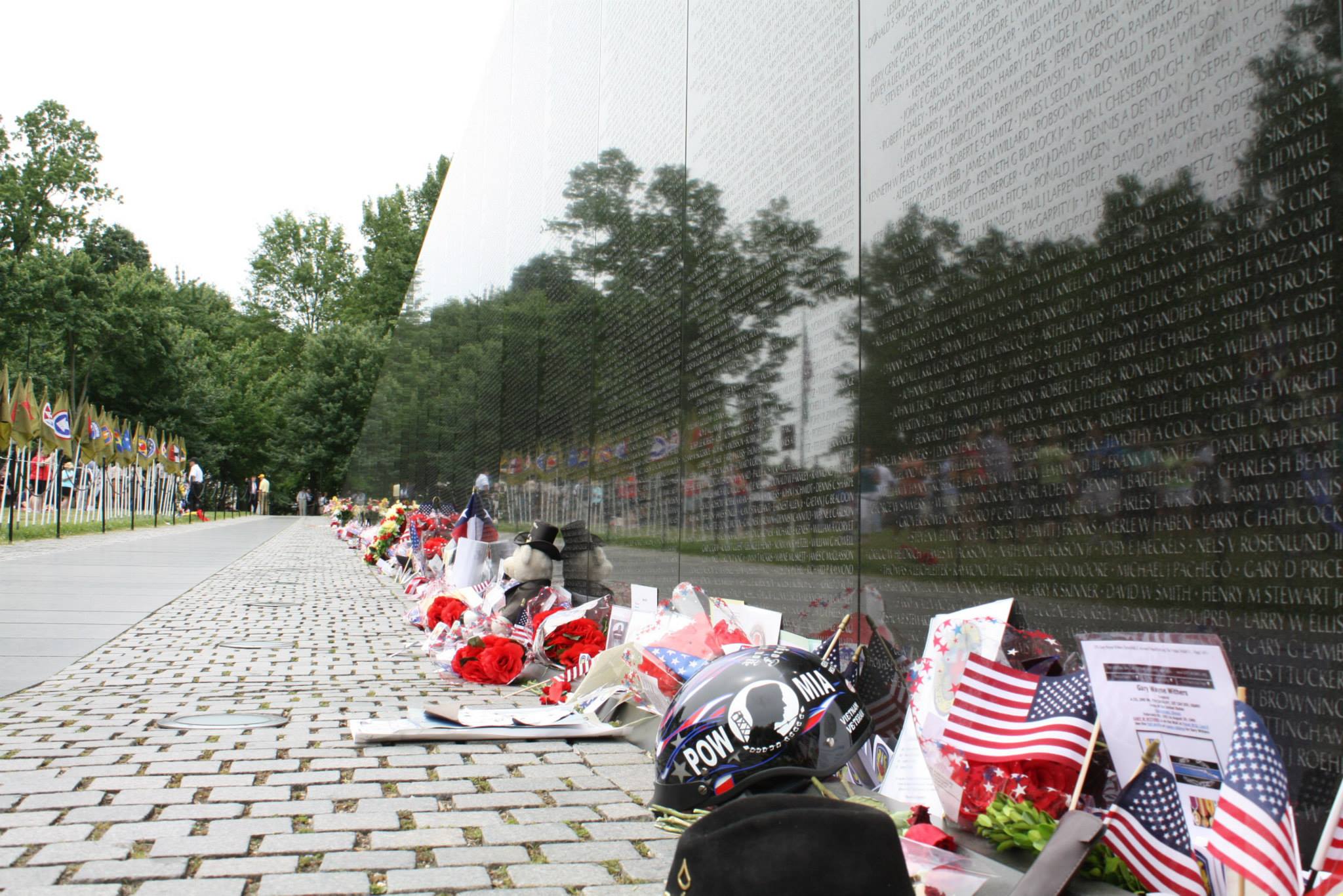 Flowers, flags, and other offerings at the base of the wall.