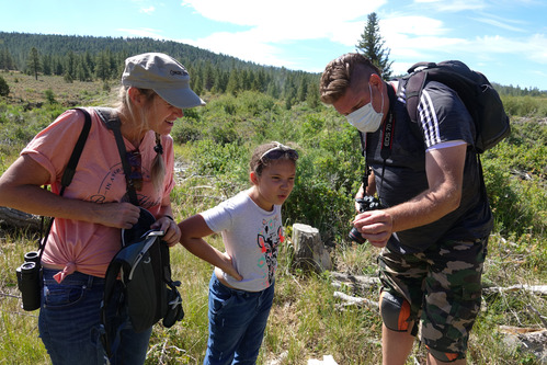 Man woman and young girl stand together to examine a butterfly held in hand
