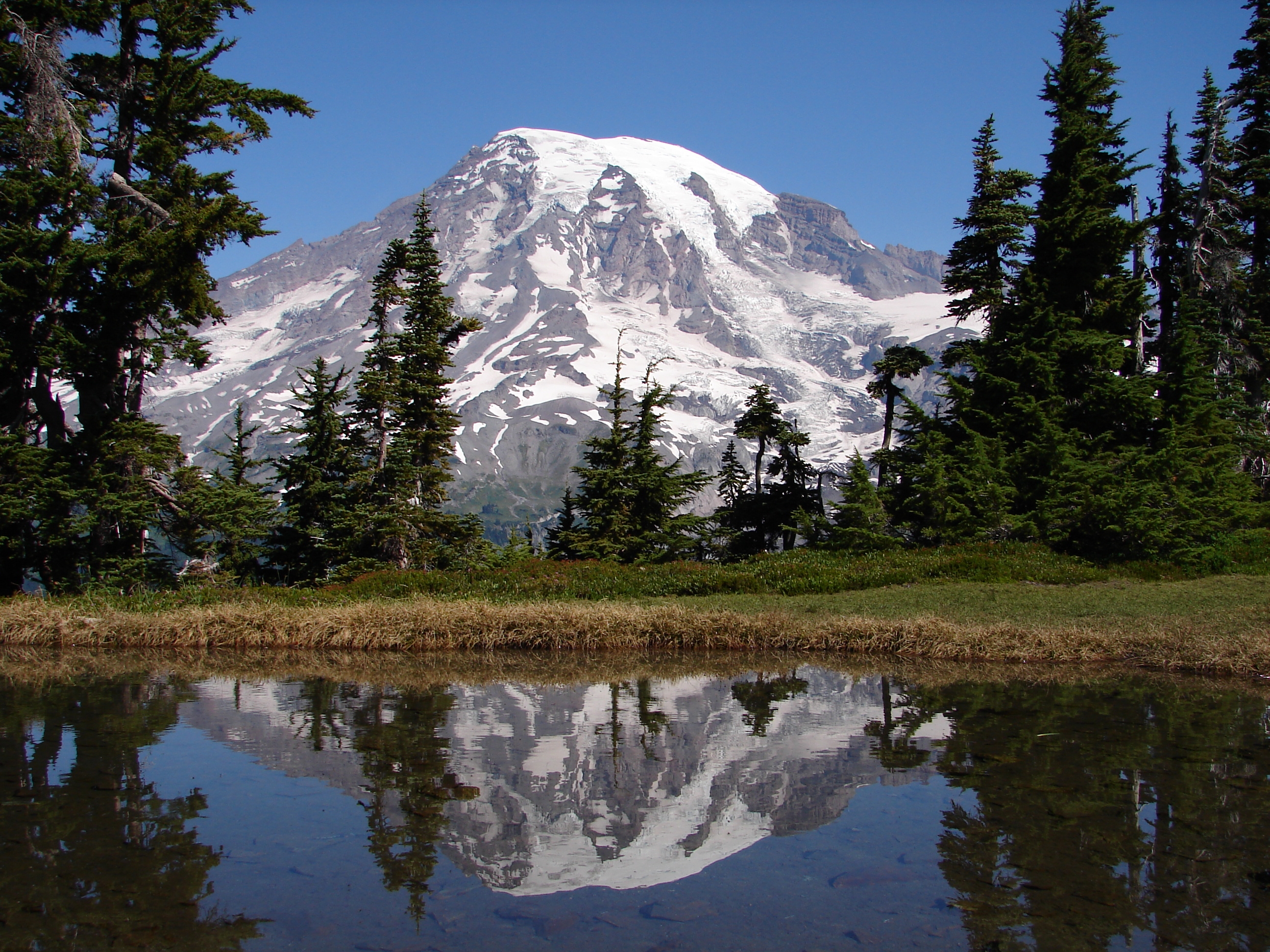 A snowy gray mountain is reflected in the lake in the foreground