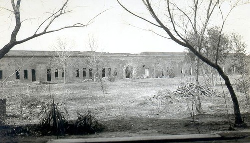 A grassy area in front of a long brick building with open windows and doors. 