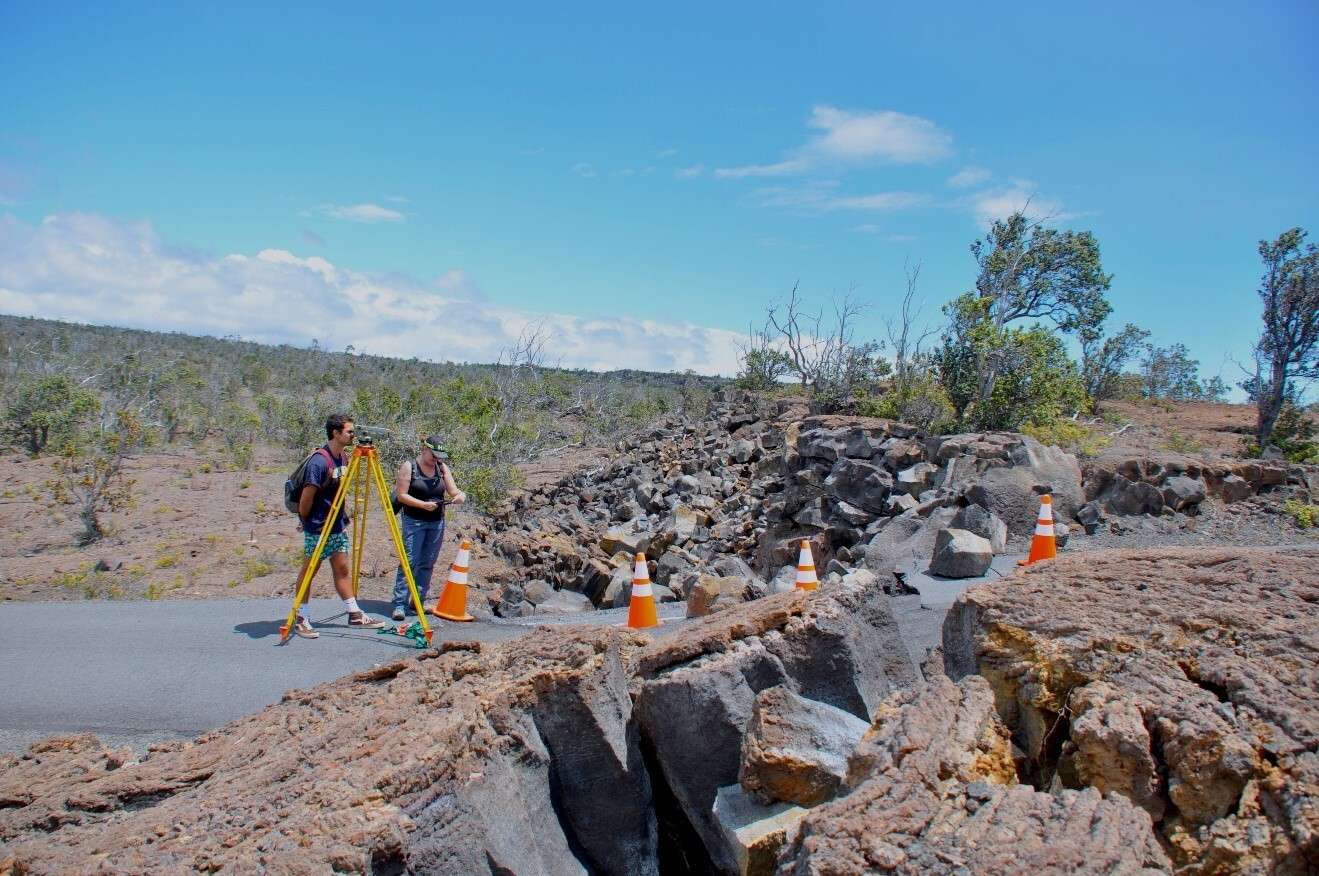 Two people use an instrument on a tripod to survey and measure a large earth crack 